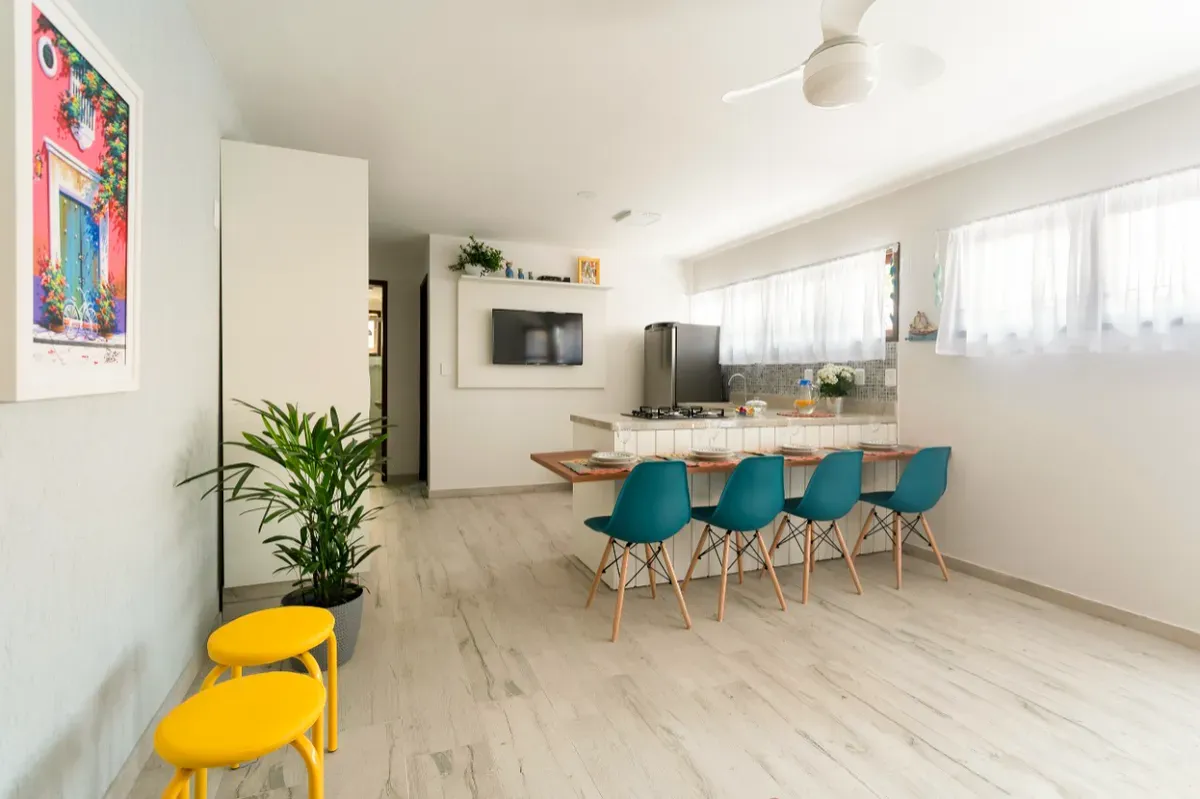 Cozinha integrada com balcão, cadeiras azul-petróleo e banquetas amarelas