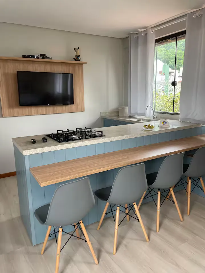 Balcão da cozinha com cooktop, banquetas e TV