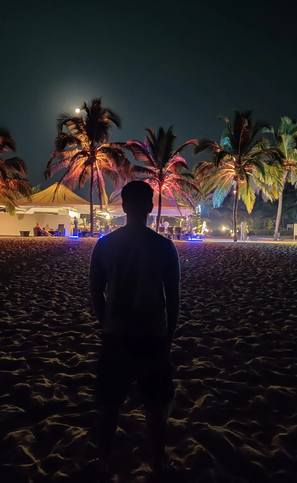 Pessoa na areia olhando um beach club iluminado à noite