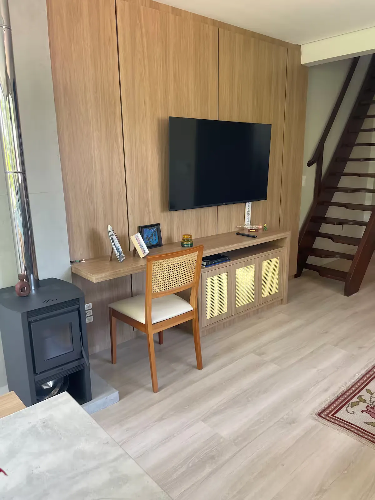 Sala com painel de madeira, TV e escada para o mezanino