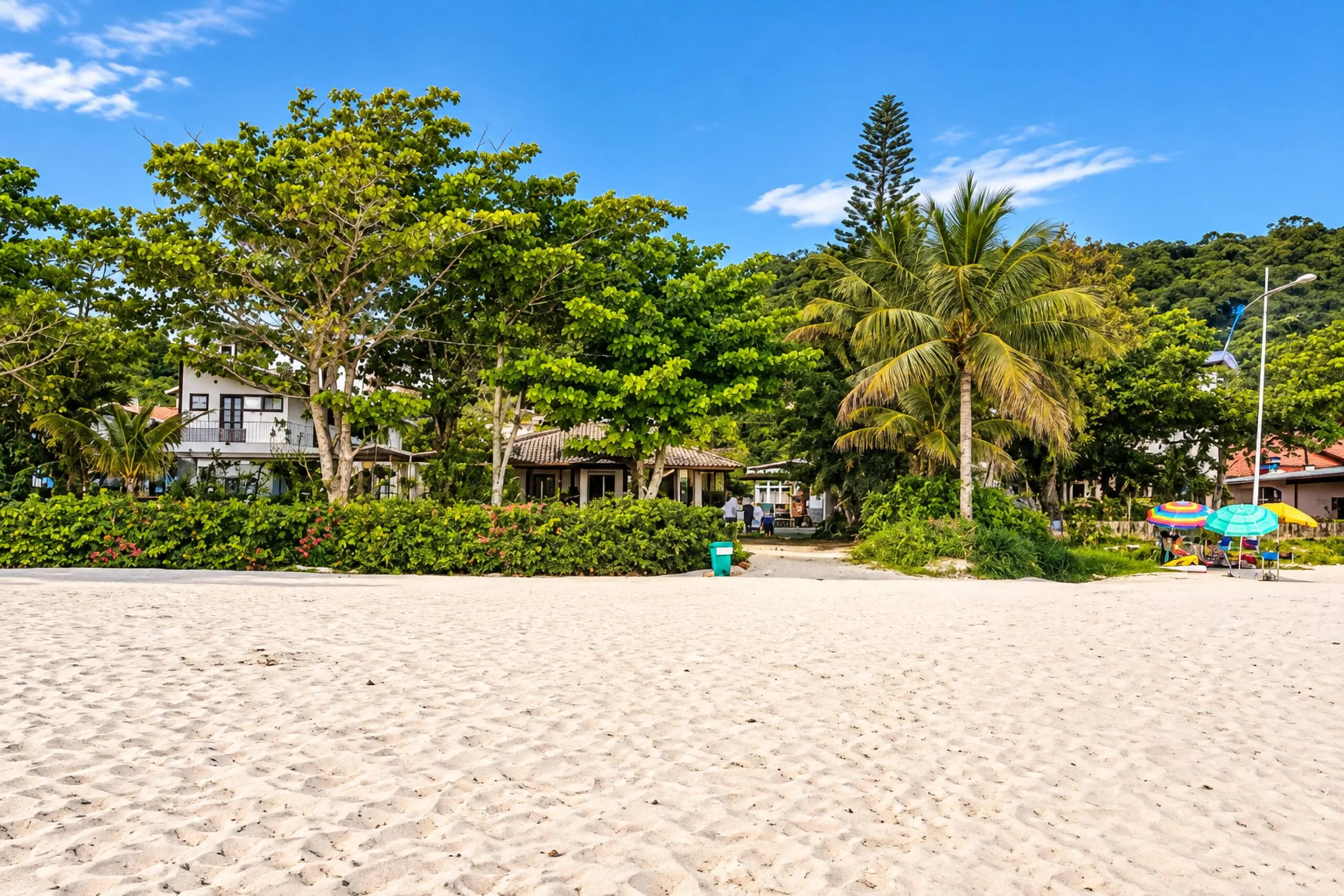 A praia de Jurerê vista da areia, com as árvores e as casas em frente ao mar